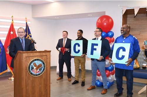 OPM Deputy Director Shriver speaks at a podium during the CFC closing ceremony. Four OPM staff stand nearby. Three of them hold a sign with the letters C, F, and C indicating the Combined Federal Campaign.